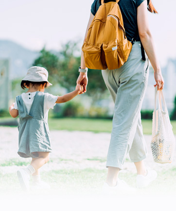 Una mujer y su hija caminando juntos por un parque soleado, rodeados de árboles.