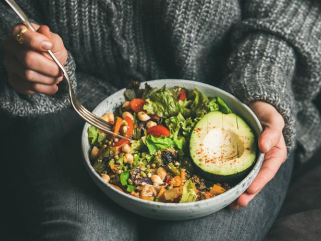 Woman holding plate of salad with avocado and vegetables