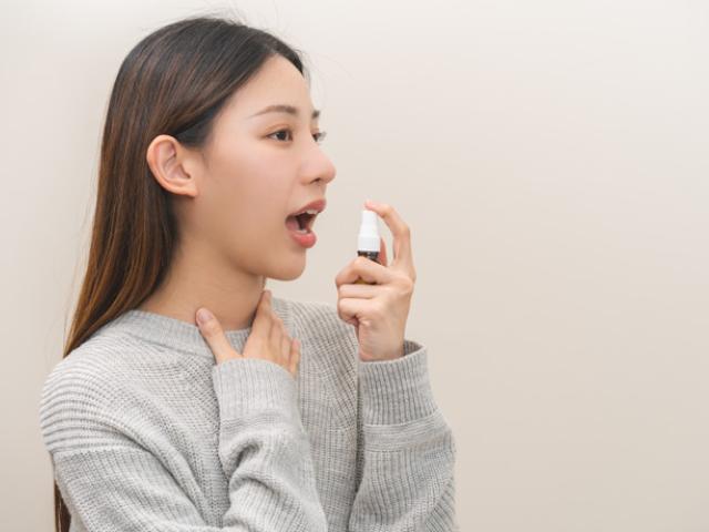 Chica echándose spray porque le salen llagas en la boca.